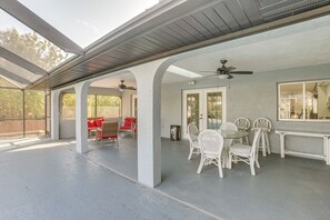 A covered patio area with white wicker furniture, a ceiling fan, and a view of the backyard.