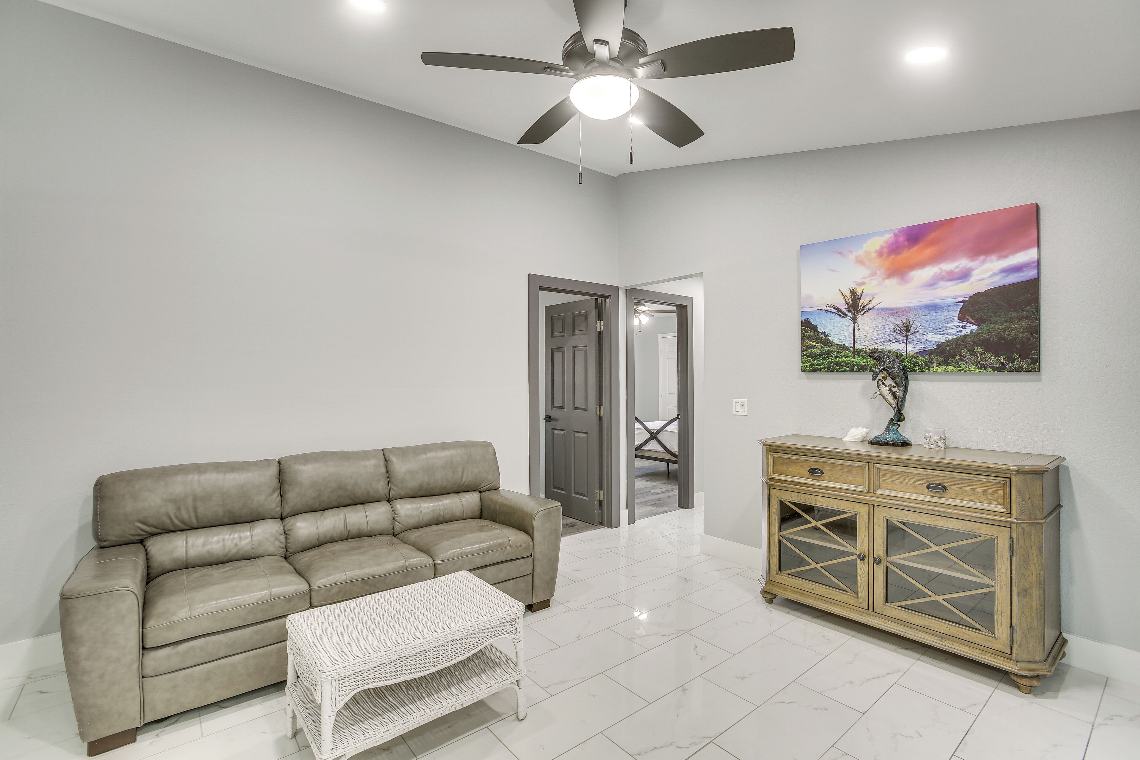 A living room with a beige sofa, a white wicker coffee table, a wooden cabinet with glass doors, and a ceiling fan.