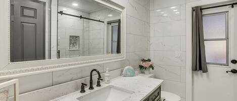 A bathroom with a marble sink, a large mirror, a toilet, and a shower area.