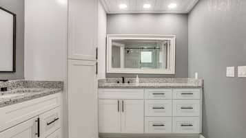 A bathroom with white cabinets, a granite countertop, and a large mirror above the sink.