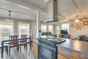 A modern kitchen with a central island, dining area with chairs, and a living space with a television and seating.