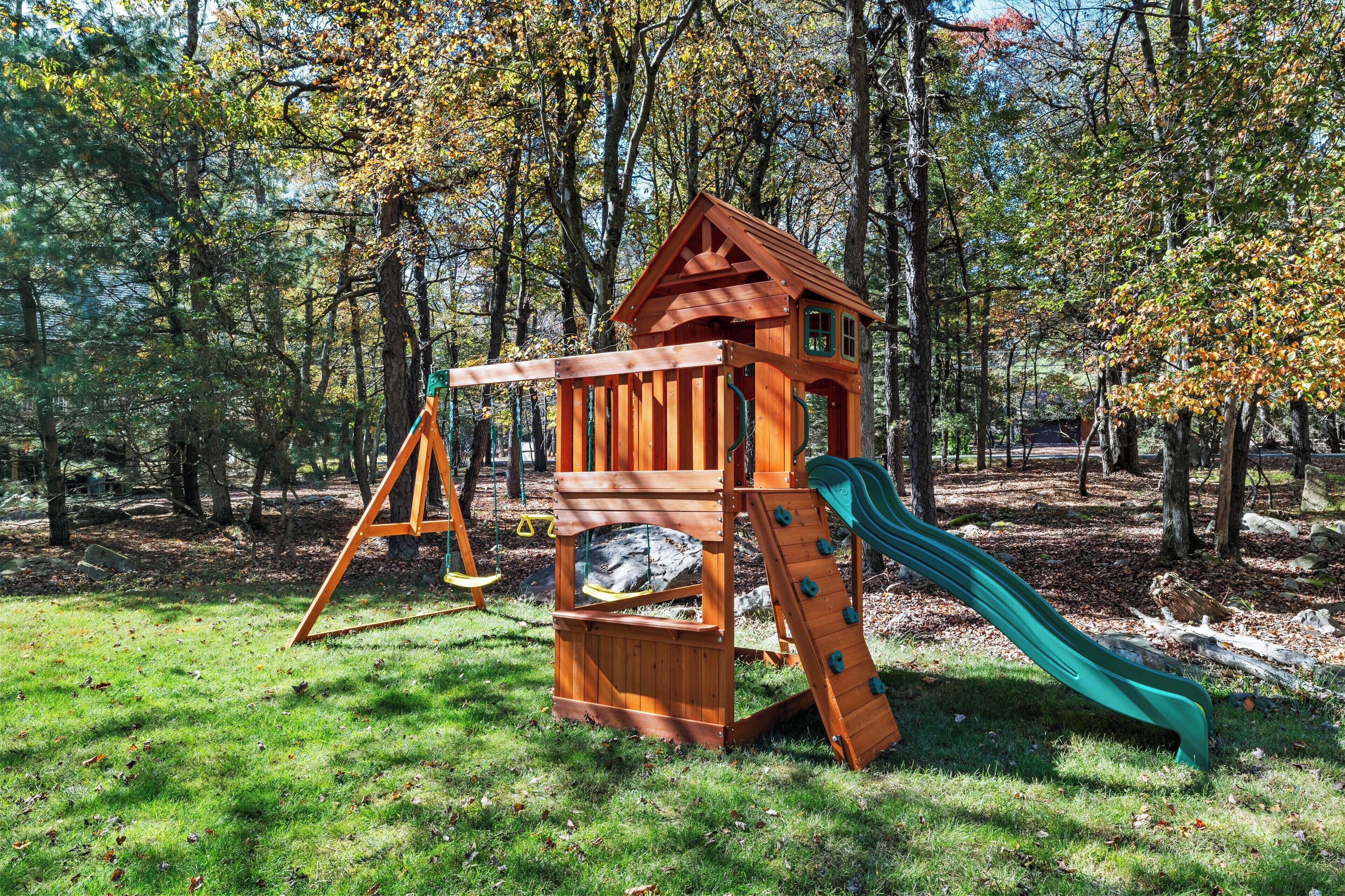 A wooden play structure with a slide and swings in a park.