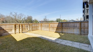 Ein Garten mit Holzzaun, gepflasterter Terrasse und Rasen.