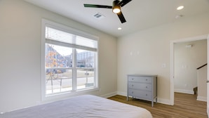 Ein Schlafzimmer mit einem großen Bett, einem Deckenventilator, einem Schminktisch und einem Fenster mit Jalousien.
