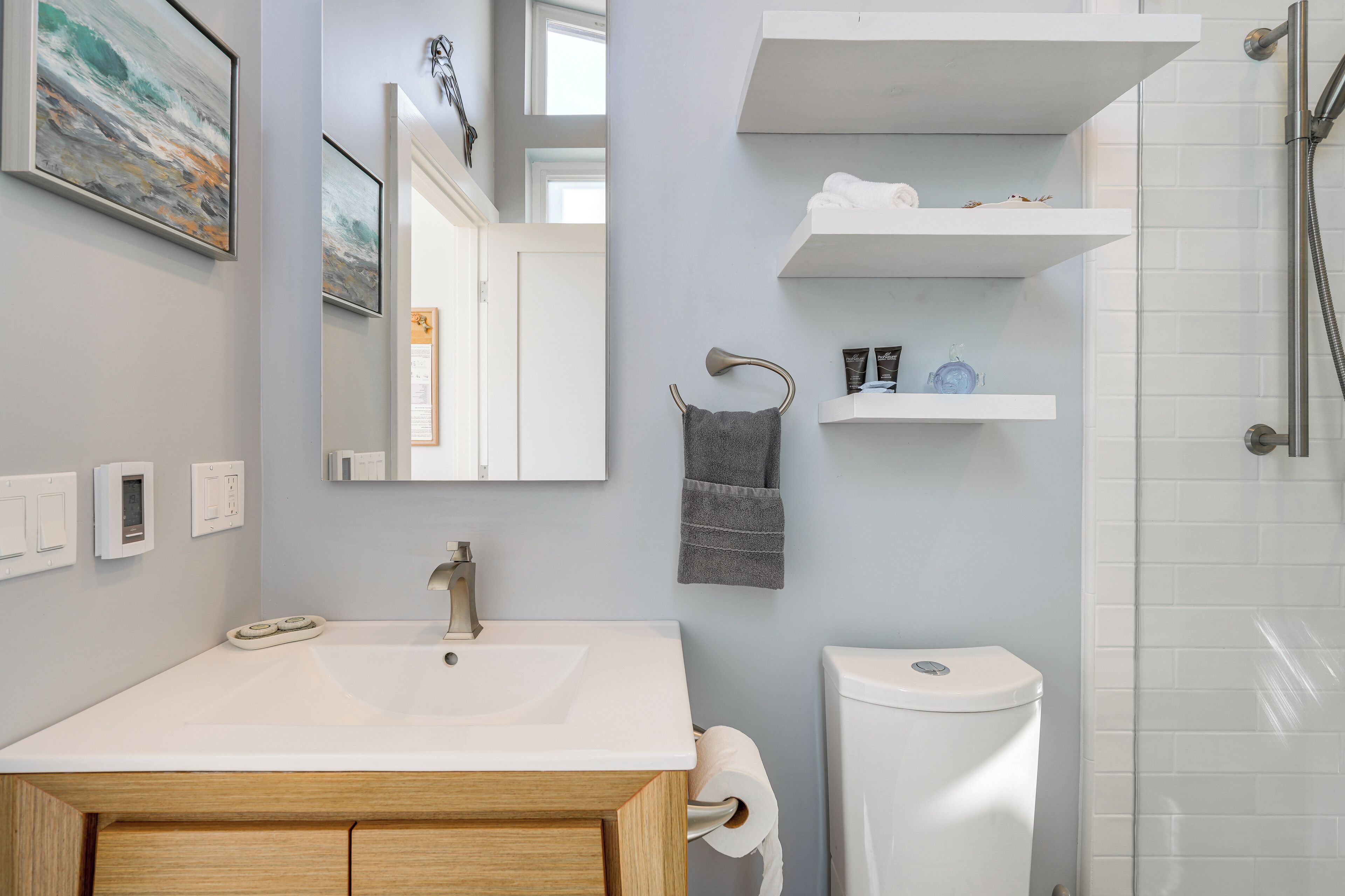 A modern bathroom with a white sink, a mirror, a towel rack, a toilet, and a shower area.