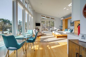 Ein modernes Wohnzimmer mit einem Glastisch, smaragdgrünen Stühlen, einer Couch und einem Bett.