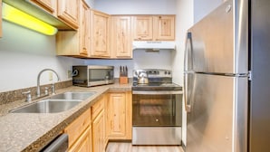 A compact kitchen with wooden cabinets, a stainless steel refrigerator, a microwave, and an oven. - Walk to Main St! Ultimate Winter Park Getaway (Winter Park)