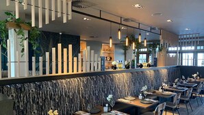 A modern restaurant with a long counter, multiple tables, and a patterned wall.