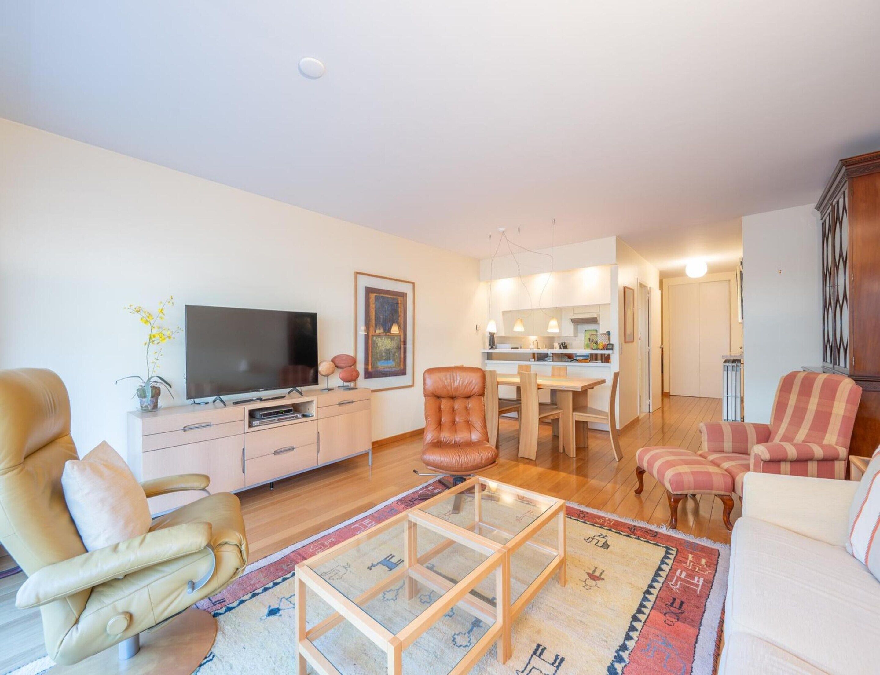Ein modernes Wohnzimmer mit Fernseher, Ledersessel und Essbereich mit Tisch und Stühlen.