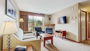 Une chambre d’hôtel avec une cheminée, une télévision, un canapé, un fauteuil, une lampe et une vue sur l’extérieur.