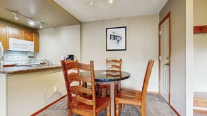 A compact kitchen with a microwave, stove, and sink. There is a dining table with four wooden chairs. A framed picture hangs on the wall above the table. - Whistler - Cascade Lodge 410 (Whistler)