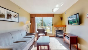 Un salon comprenant un canapé, un fauteuil, une table basse, une cheminée, un téléviseur et un balcon avec vue.
