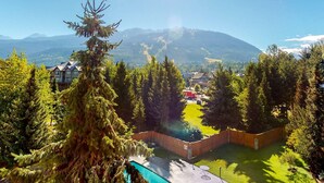 Un quartier résidentiel doté d’une piscine, entouré de grands arbres et bordé par une chaîne de montagnes.