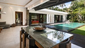 A modern house with a glass dining table, a pool, and a view of the garden. - Elegant 3BR Oasis in the Heart of Seminyak (Kuta Utara)