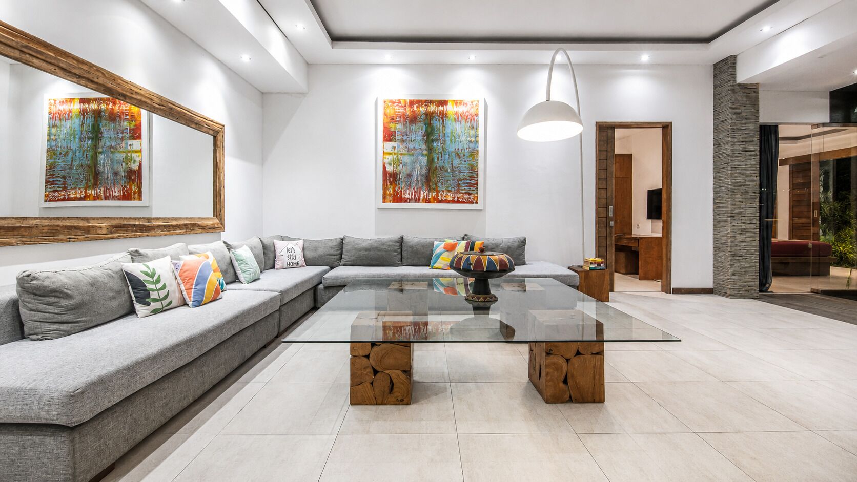 Een moderne woonkamer met een glazen salontafel, een grijze bank en abstracte schilderijen.