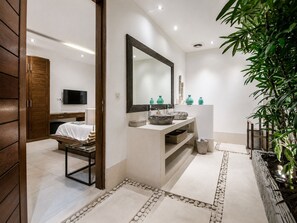 A modern bathroom with a large mirror, a sink with decorative bowls, a television in the background, and a plant on the right. - Elegant 3BR Oasis in the Heart of Seminyak (Kuta Utara)