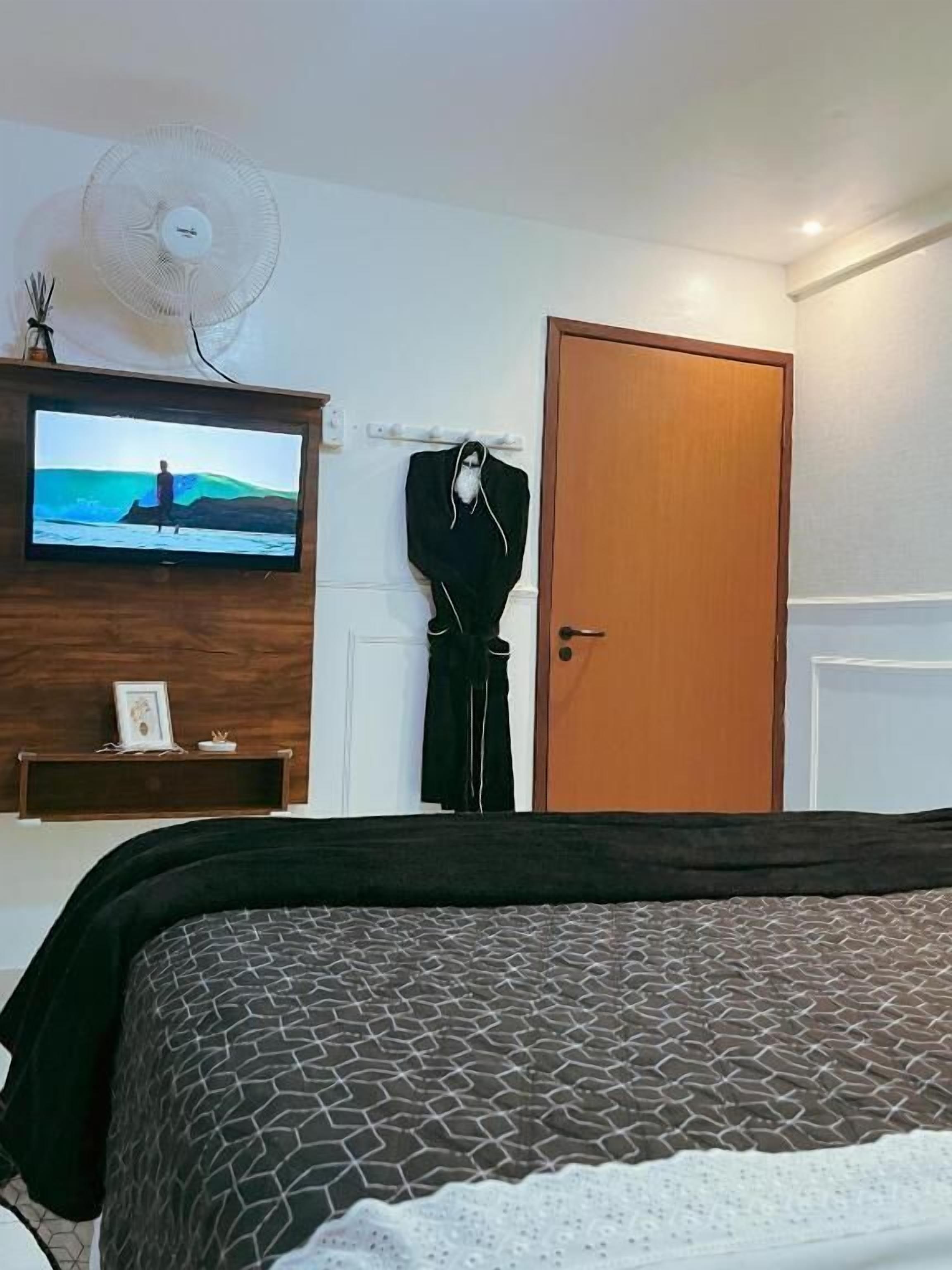 A bedroom with a bed, a television on the wall, a door, and a wall-mounted fan.