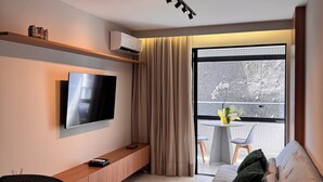 A modern living room with a flat-screen TV, a sofa, a wooden console table, and a dining area with a table and chairs. - Cozy NEW apartment in Ondina (Salvador)