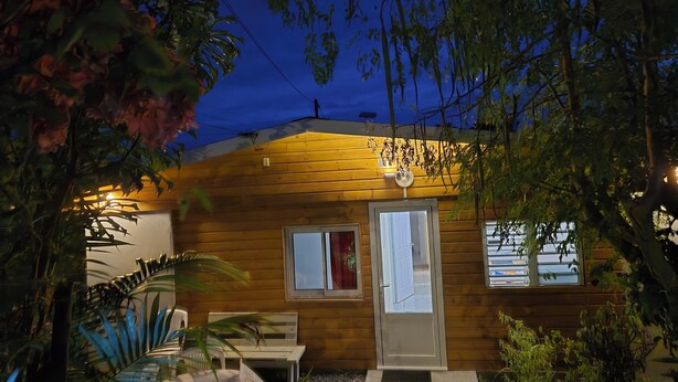 A wooden cabin with a door and windows, surrounded by plants and a bench. - Chalet les planifolias, landscaped garden, access to numerous paths, sea and mountains. (Saint-Philippe)