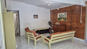 A room with a wooden wall, a white ceiling, a bench, a table, and a fan. - Chalet les planifolias, landscaped garden, access to numerous paths, sea and mountains. (Saint-Philippe)