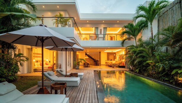 Un área moderna junto a la piscina con sillones de descanso, sombrillas y una terraza de madera.