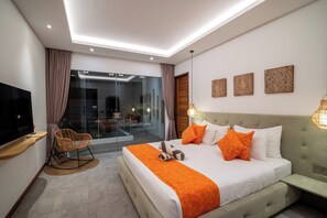 Habitació d'hotel moderna amb un llit gran, una televisió, zona de seients i una porta de vidre que dona a un balcó.