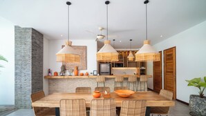 Un comedor con mesa de madera, sillas de mimbre e iluminación colgante de mimbre.