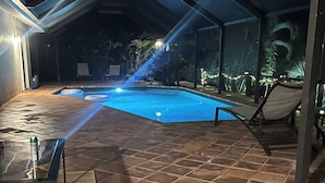 An outdoor swimming pool with a tiled deck, lounge chairs, and a covered area with a view of the pool.