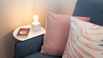 Ein gemütlicher Winkel mit einem blauen Sofa, einem kleinen weißen Beistelltisch, einem Buch und einer beleuchteten Lampe.