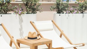 Eine Dachterrasse mit zwei Holzliegen, einem kleinen Tisch und einem Hut.