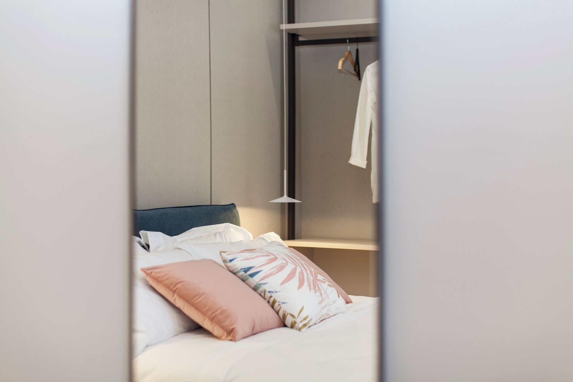 A neatly made bed with pillows, a hanging light fixture, and a clothing rack in a modern room.