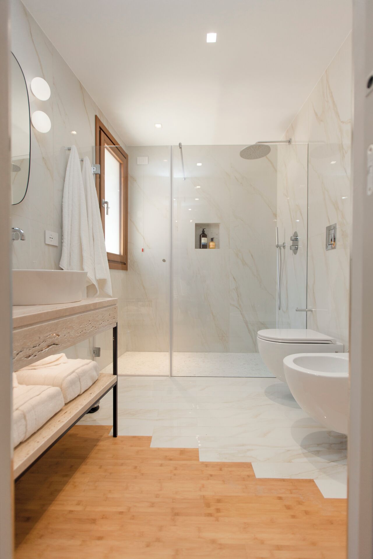 A modern bathroom with a glass-enclosed shower, a large bathtub, and a vanity with a mirror and towel rack.