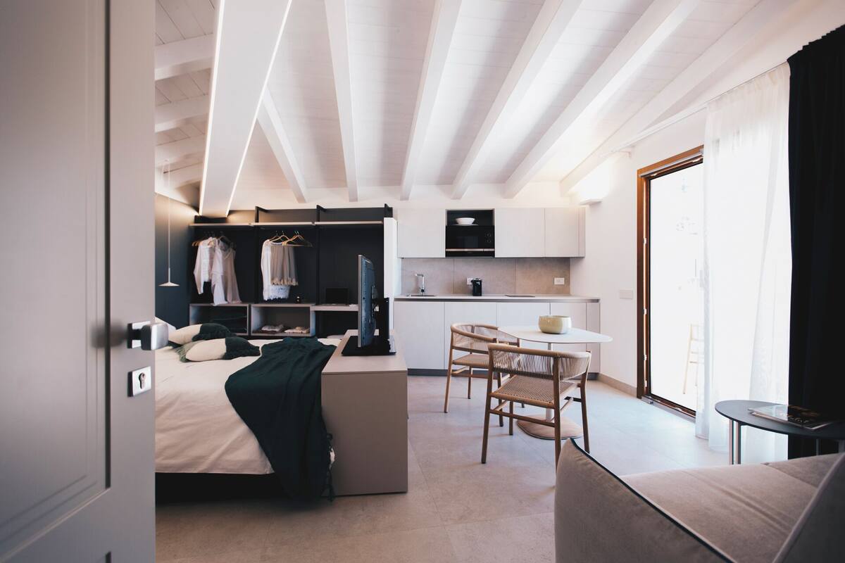 Una habitación de hotel moderna con cama, zona de estar, kitchenette y armario.