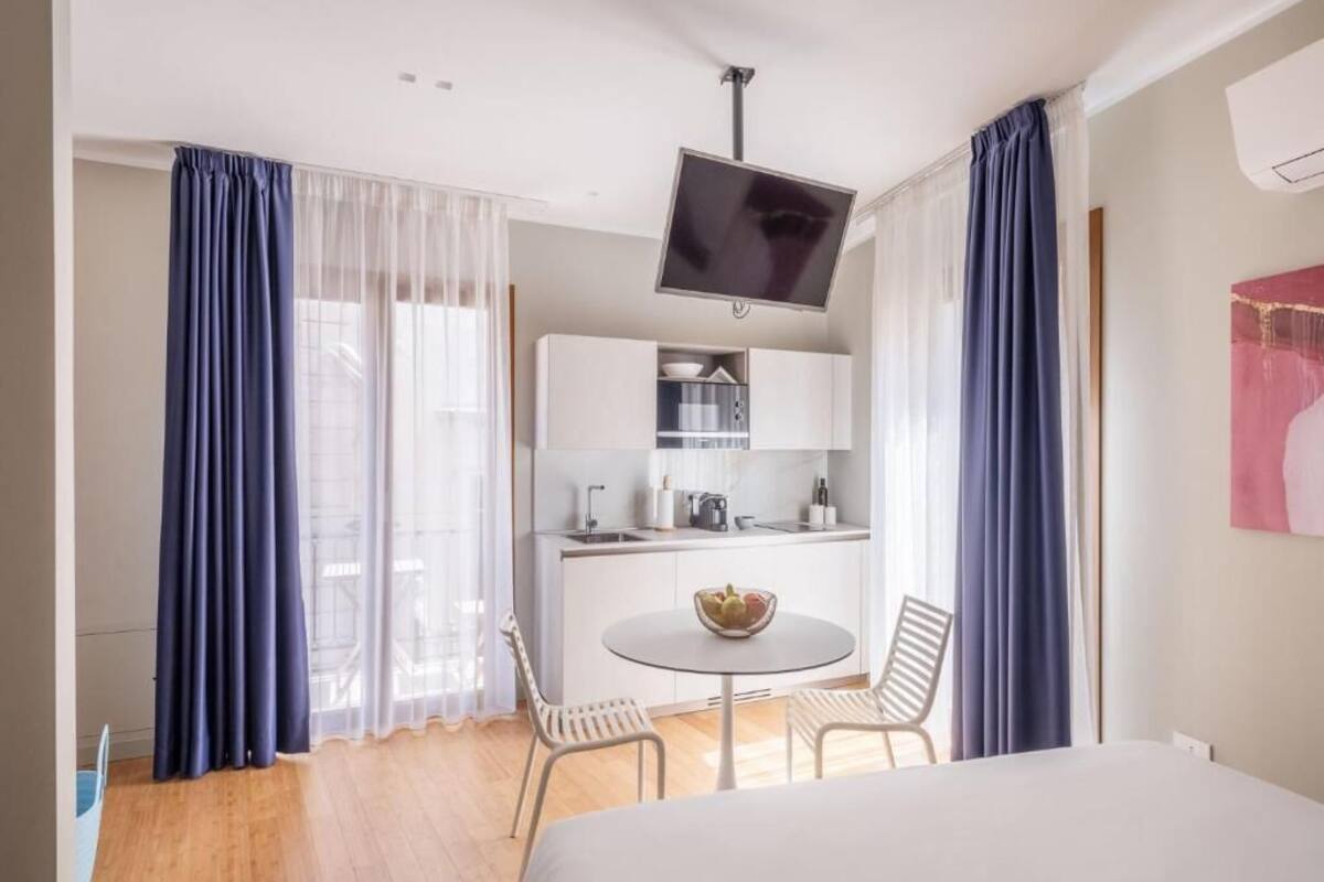 Una habitación de hotel con una cama, una pequeña mesa de comedor con sillas, una kitchenette y un televisor en la pared.