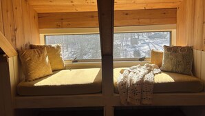 Een blokhut met twee houten banken met kussens, een raam met uitzicht op een besneeuwd bos en een houten plafond.