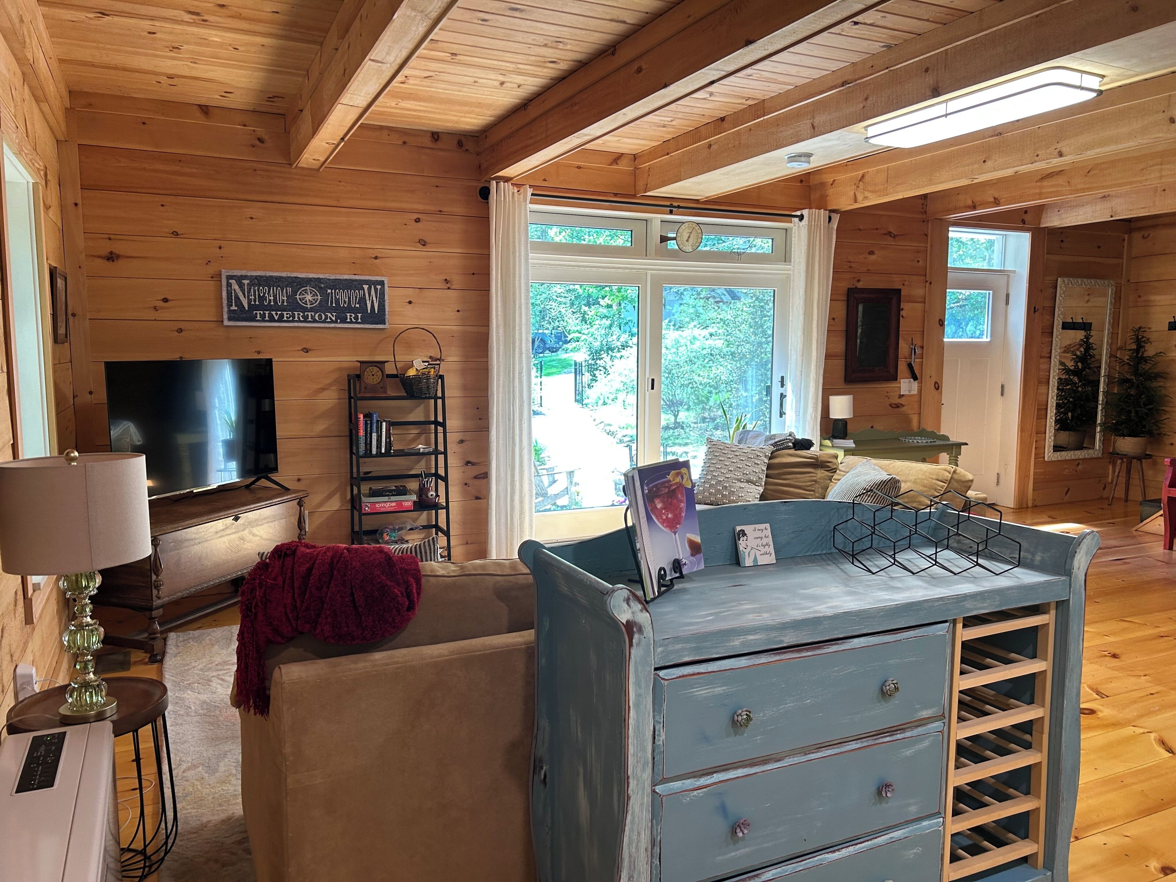A cozy cabin interior with a television, bookshelf, and a large window offering a view of the outdoors.