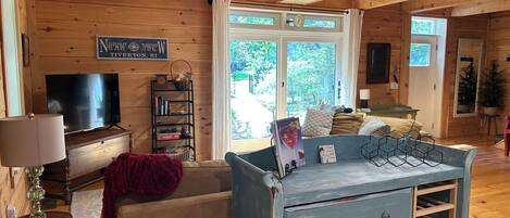 A cozy cabin interior with a television, bookshelf, and a large window offering a view of the outdoors.