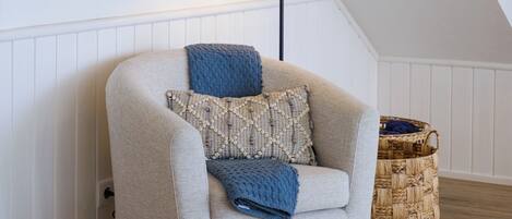 A cozy living room with a beige armchair, a blue throw blanket, and a woven basket on the floor.