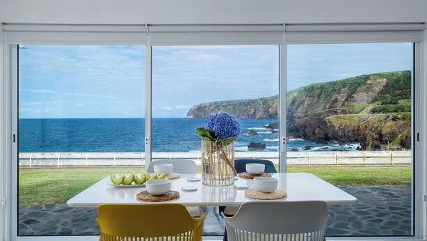 Ein Esstisch mit Blick aufs Meer, eine Vase mit blauen Blumen und eine Obstschale.