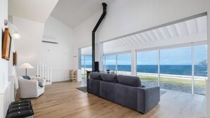Ein geräumiges Wohnzimmer mit grauem Sofa, Holzböden und einem großen Fenster mit Meerblick.