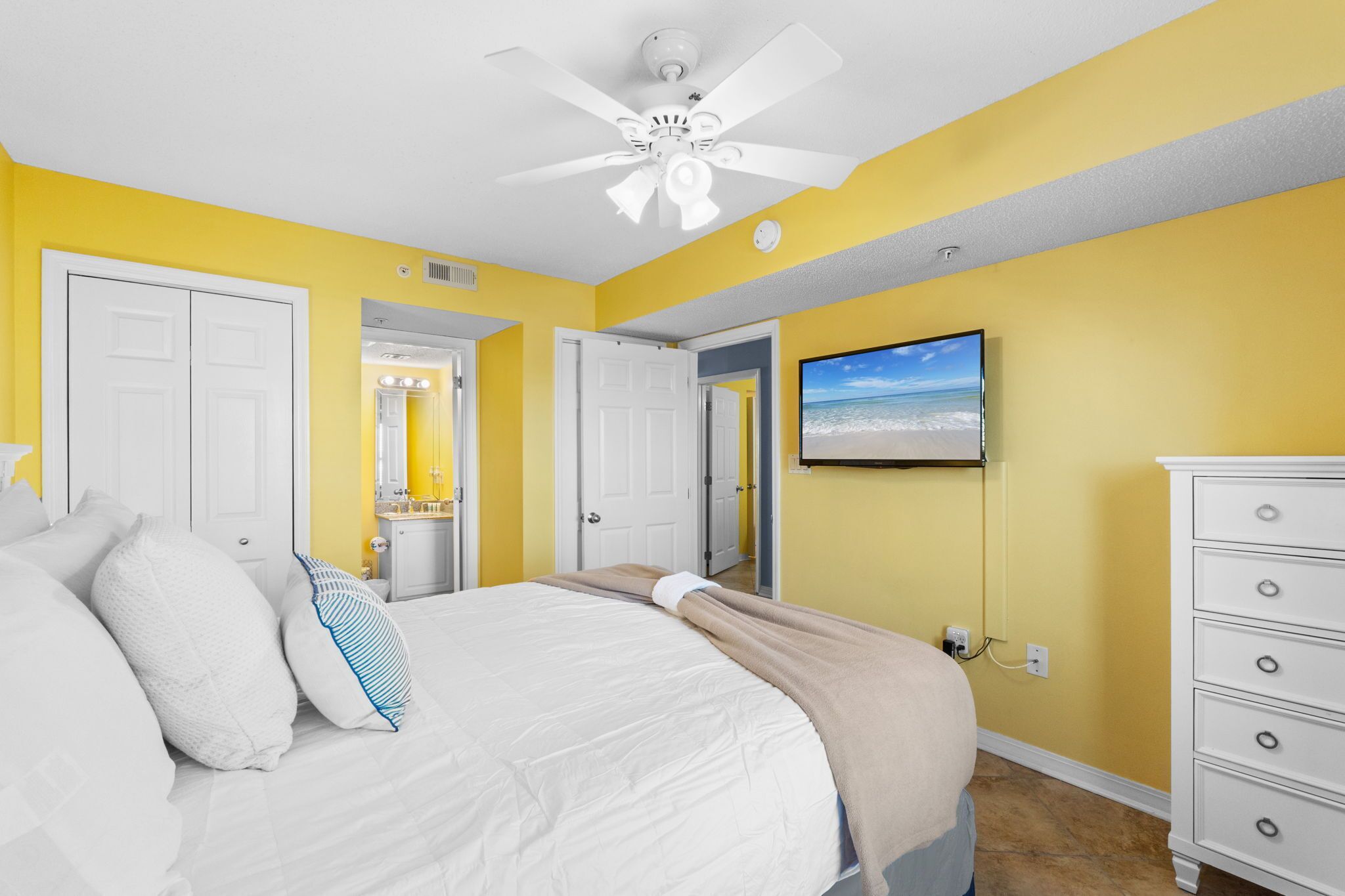 Une chambre à coucher avec un lit, une commode blanche et un ventilateur de plafond.