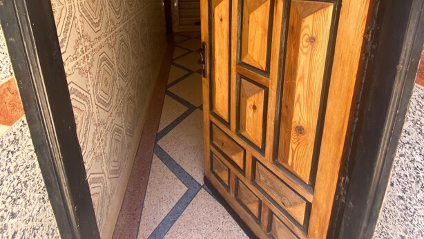 Un couloir aux murs ornés de motifs et une porte en bois aux motifs géométriques.