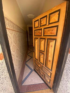 Un pasillo con paredes de diseño y una puerta de madera con motivos geométricos.