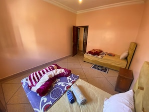 A room with a bed, a chair, a small table, and a door leading to another room.