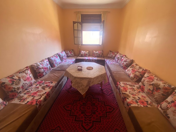 A room with a central round table, floral-patterned sofas arranged around it, and a patterned carpet.