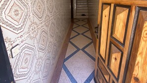 Un couloir aux murs ornés de motifs et au sol présentant un dessin géométrique, qui mène à une porte dont le panneau est en bois.