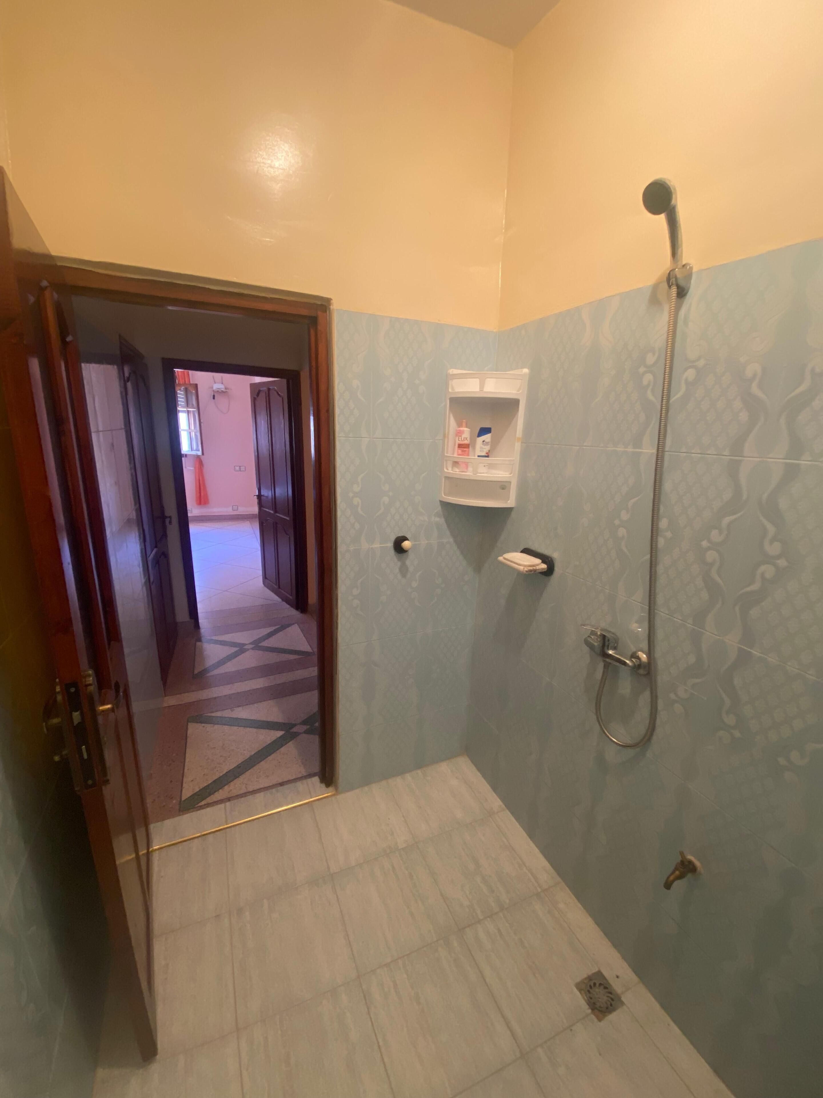 Un baño con ducha, toallero y repisa con artículos de aseo.