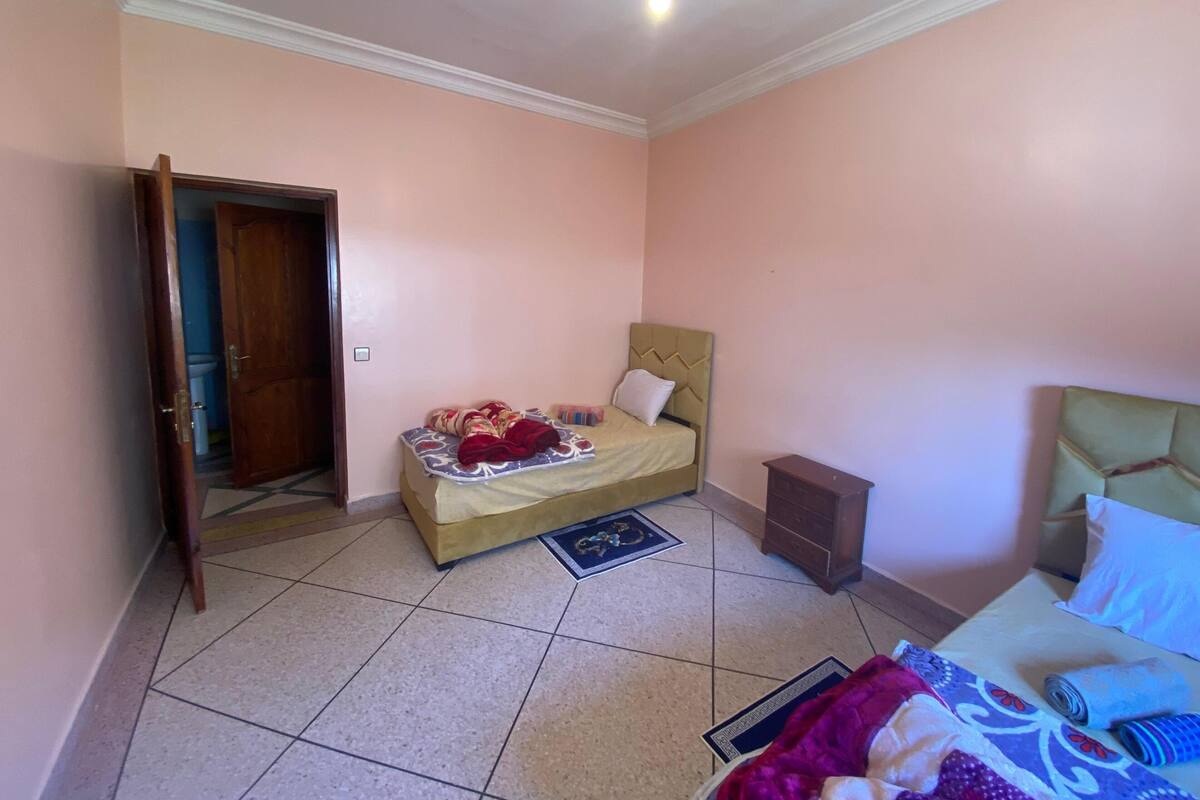 A bedroom with a bed, a nightstand, a wooden door, and a tiled floor.