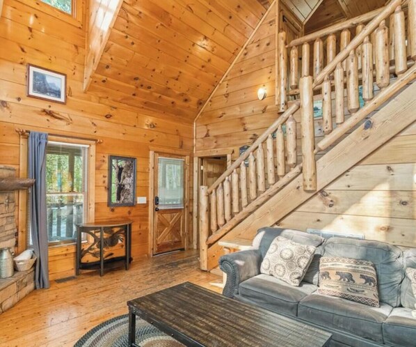 A wooden cabin interior with a staircase, a sofa, a table, and a door. - Private Hot Tub | Pool Table | 15mins to PF & Gatlinburg (Sevierville)