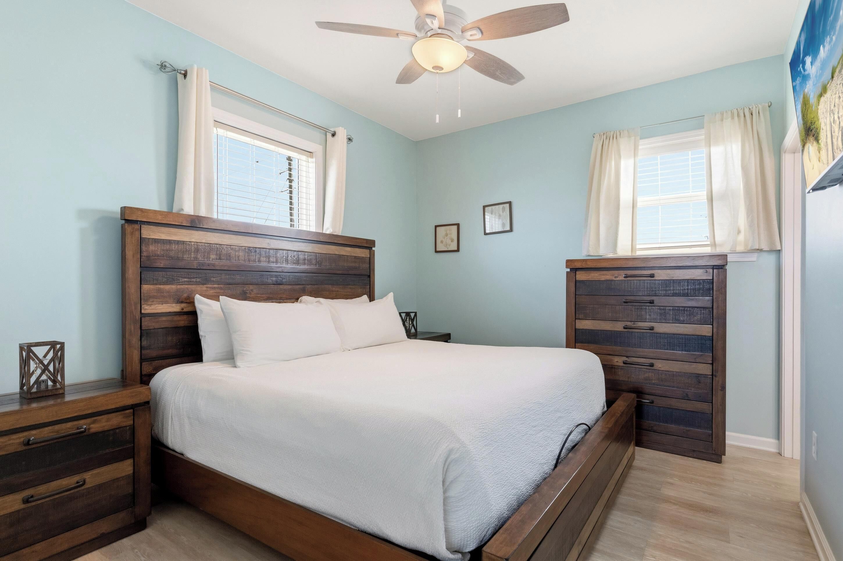 A bedroom with a wooden bed, nightstands, a ceiling fan, and a window with curtains.